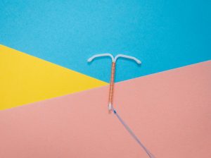 an IUD (coil) lies on a blue, pink and yellow background
