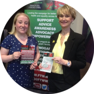 Carly and Lara stand next to the FTWW exhibition stand, holding FTWW flyers