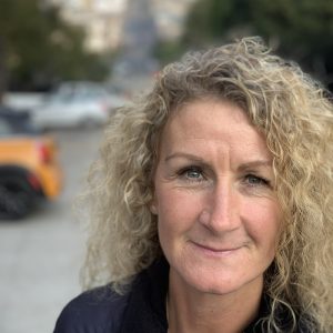 Lisa, a white woman with blonde curly hair is smiling at the camera.