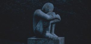 A stone statue of a person sat wrapping their arms around their shins, resting their head on their knees.